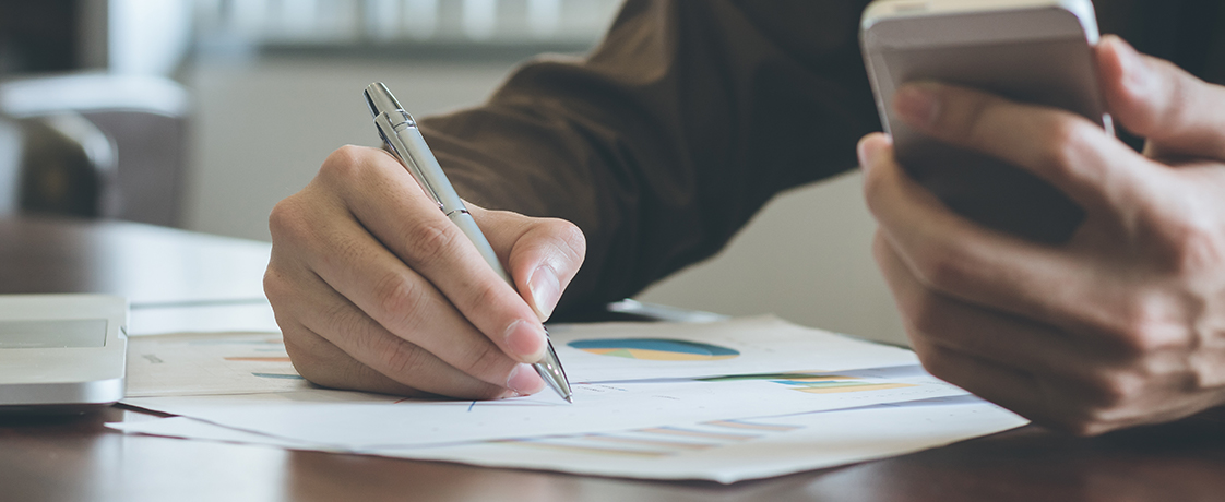 A person writing and holding a calculator